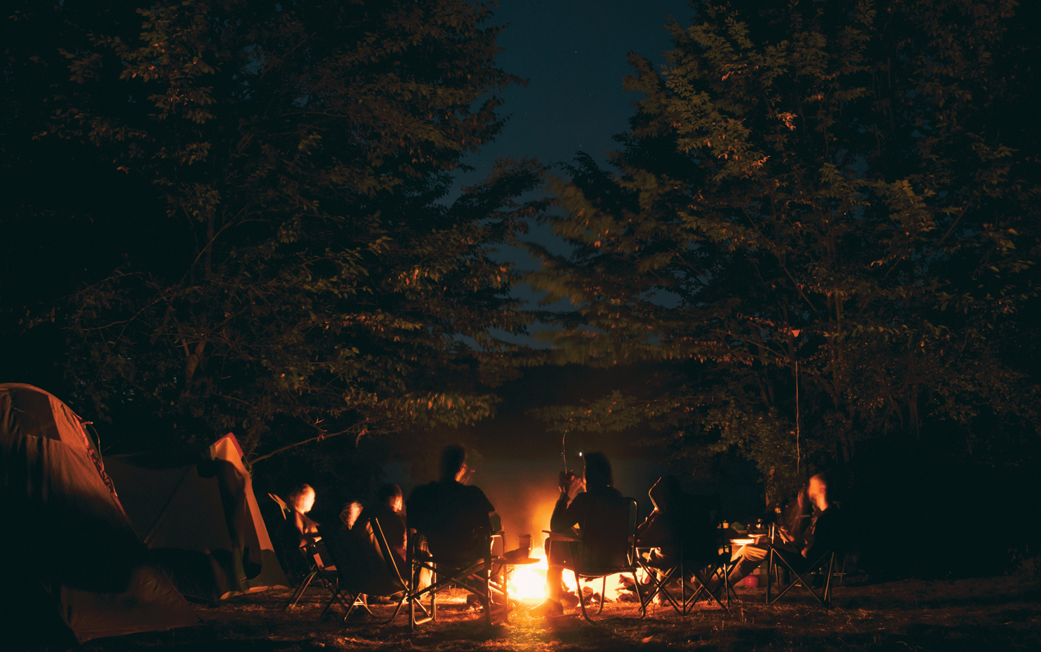 A group of people sitting around the fire at night.